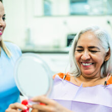 Woman smiling at her reflection with a dentist watching